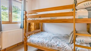 A bunk bed with a wooden frame, a radiator, a window with curtains, and a view of greenery outside. - 2 Bed in Bideford (oc-76507) (Bideford)