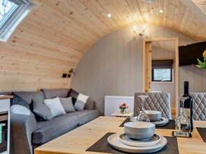 A cozy room with a wooden ceiling, a grey sofa, a dining table with plates and glasses, and a TV mounted on the wall.