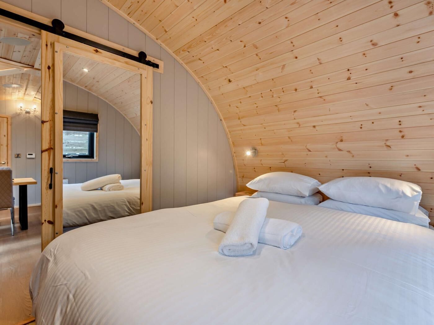 Une chambre confortable avec un plafond cintré, un lit recouvert de draps blancs et une porte en bois.