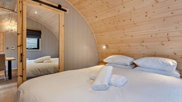 Une chambre confortable avec un plafond cintré, un lit recouvert de draps blancs et une porte en bois.