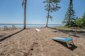 A beach with two lounge chairs, a blue and white board game, and a book on the sand.