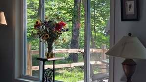 Una ventana con un jarrón de flores, una lámpara y una silla de madera en el exterior.