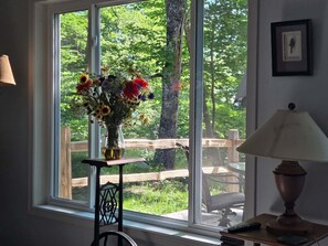 Ein Fenster mit einem Blumenstrauß, einer Lampe und einem Holzstuhl davor.