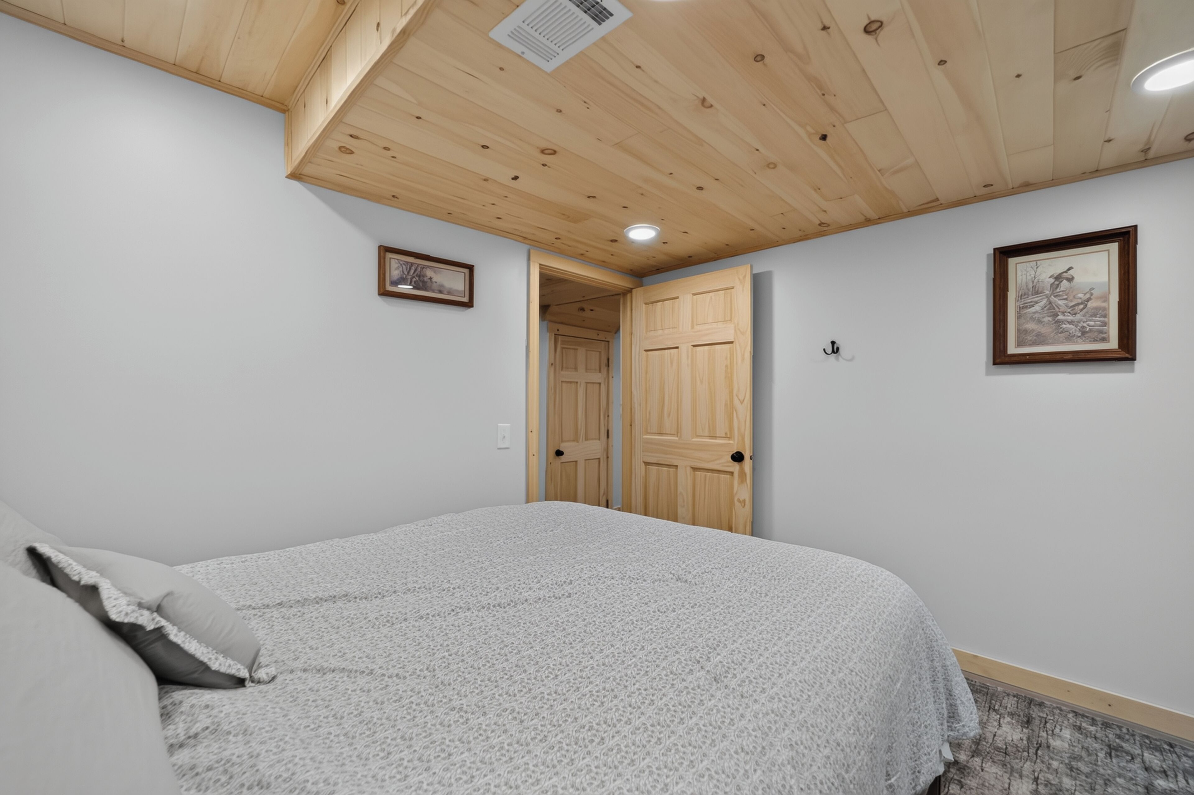 A bedroom with a bed, a wooden ceiling, a door, and a framed picture on the wall.