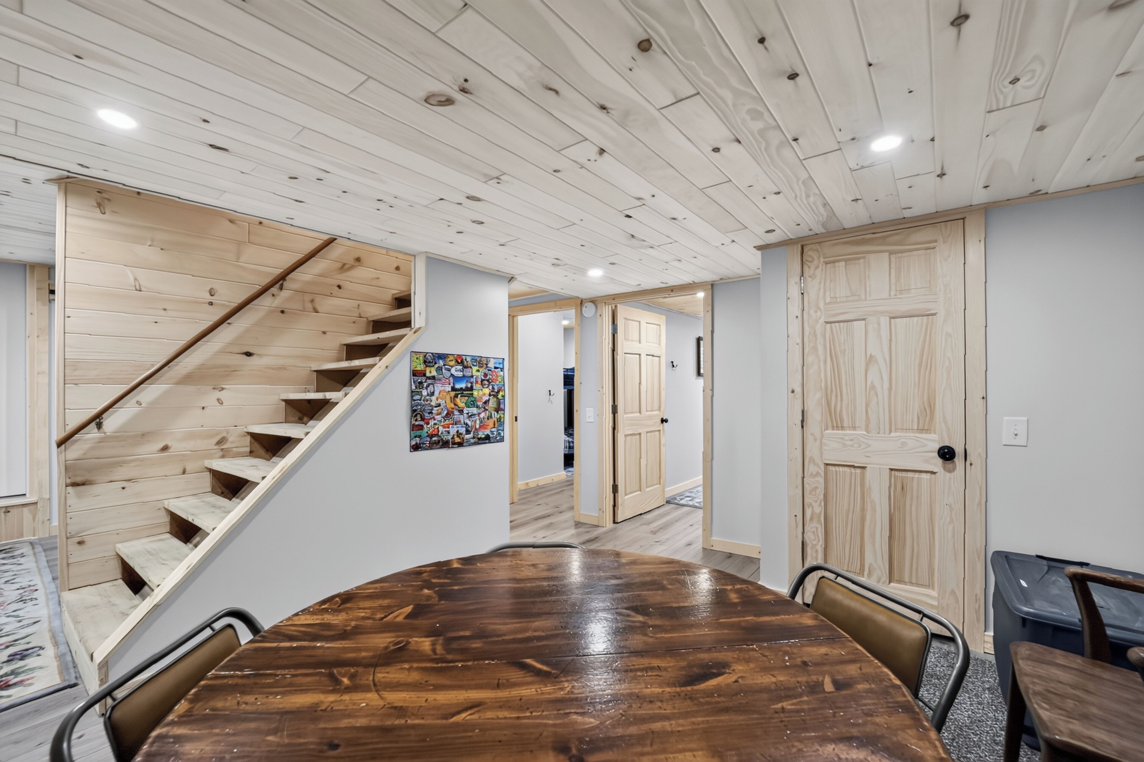 A wooden staircase leading to a second floor, a dining area with a large wooden table, and a door with a wooden panel design.