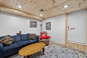 A room with a blue sofa, a wooden coffee table, a red chair, and a door with an emergency exit sign. - Gaylord Lodge:  Fall Color Getaway | Gaylord | 4BR Forest Retreat | Sleeps 8 (Gaylord)