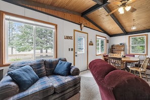 A cozy lodge interior with a wooden ceiling, large windows, a sofa, a dining table, and a red chair. - Gaylord Lodge:  Forest Escape: Golf, Ski, Fish and Sleep 8! (Gaylord)