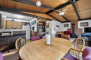 A cozy interior with a wooden dining table, chairs, a kitchen area, and a living room with a fireplace. - Gaylord Lodge:  Fall Color Getaway | Gaylord | 4BR Forest Retreat | Sleeps 8 (Gaylord)