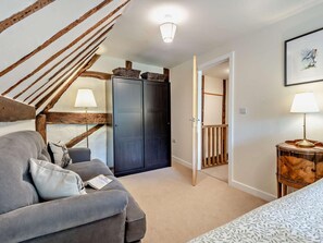 Ein gemütliches Zimmer mit grauem Sofa, einer Holztreppe, einem Kleiderschrank und einem Bett mit gemustertem Überwurf.
