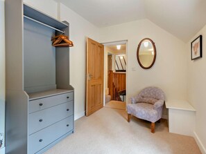 Ein Zimmer mit grauem Kleiderschrank, einer Holztür, einem runden Spiegel und einem gemusterten Sessel.