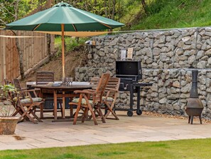 Eine Terrasse im Freien mit Tisch, Stühlen, einem Grill und einer Steinsäule.