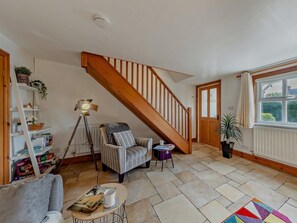 A living room with a wooden staircase, a bookshelf, a floor lamp, a striped armchair, a coffee table, and a window with a view. - 2 Bed in Kelsall (oc-94445) (Kelsall)