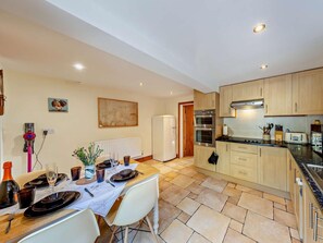 A modern kitchen with wooden cabinets, a built-in oven, and a dining area with a table set for two. - 2 Bed in Kelsall (oc-94445) (Kelsall)