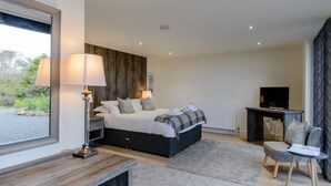 A modern bedroom with a bed, bedside lamps, a TV, a small table, and a view of greenery outside. - 3 Bed in Belford (oc-78058) (Easington)