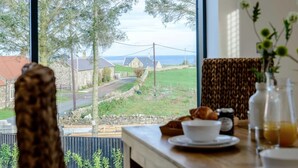 A dining area with a view of a rural landscape, stone buildings, and a body of water. - 3 Bed in Belford (oc-78058) (Easington)
