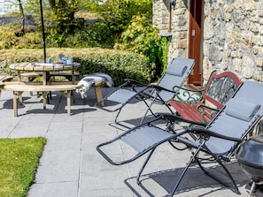 An outdoor seating area with a stone wall, a wooden table, and metal chairs. - 3 Bed in Bodmin (oc-herti) (Bokiddick)