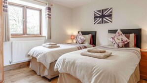 Ein Doppelzimmer mit zwei Betten, einem Fenster mit Vorhängen, einem Heizkörper, einer Lampe und einer Wand mit einer Union Jack Flagge.