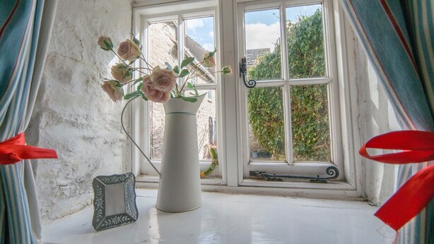 A window with a white vase containing flowers, a small framed picture, and a window handle.