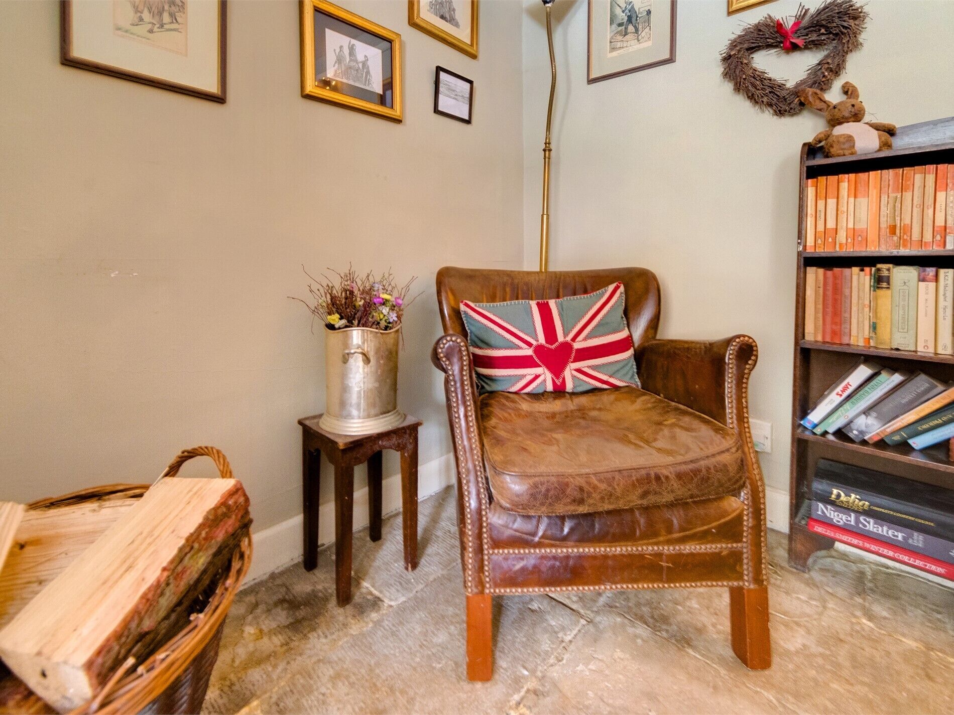 Ein Ledersessel mit Kopfkissen mit Union Jack, ein Bücherregal mit Büchern, ein kleiner Tisch mit einem Metallbehälter und gerahmte Kunstwerke an der Wand.