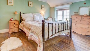 A bedroom with a four-poster bed, a wooden dresser, a nightstand with a lamp, and a large window with a view.