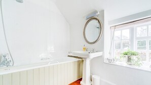 A bathroom with a bathtub, a sink, a mirror, and a window with plants.