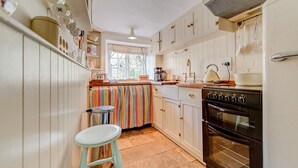 A kitchen with white cabinets, a black stove, a striped cloth over the counter, and a stool.