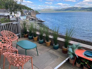 Eine Terrasse mit Gartenmöbeln, Kübelpflanzen und Blick auf einen See und Hügel.