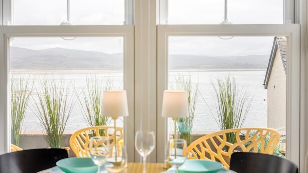 A table set for two with chairs, a view of a body of water, and a building in the background. - 2 Bed in Aberdyfi (oc-dy020) (Aberdovey)