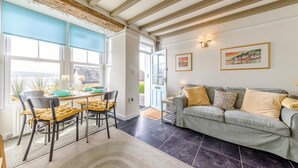 A room with a dining table, chairs, a sofa, and a view through large windows. - 2 Bed in Aberdyfi (oc-dy020) (Aberdovey)