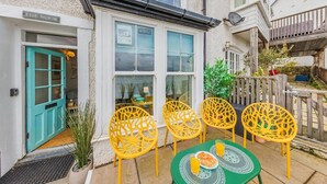 A patio with yellow chairs and a table, a turquoise door, and a white building with a window. - 2 Bed in Aberdyfi (oc-dy020) (Aberdovey)