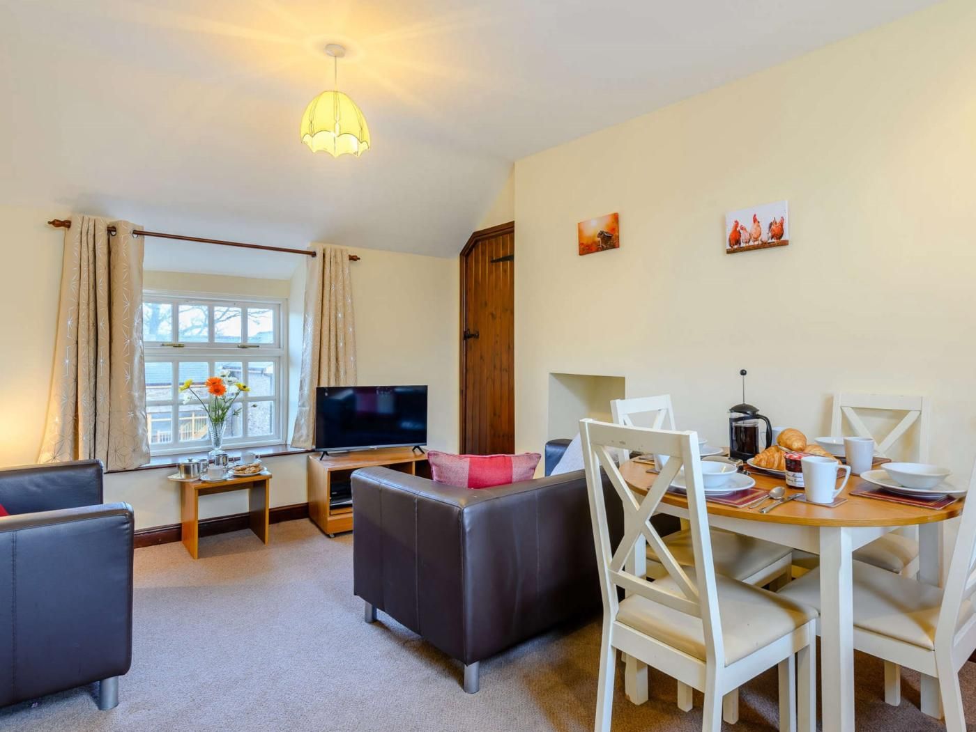 Een gezellige woonkamer met een bank, een televisie, een eettafel met stoelen en een raam met gordijnen.