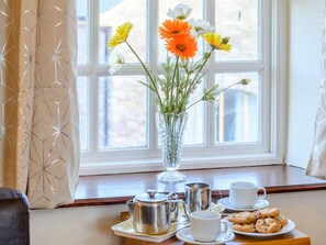 A window with a view of buildings, a vase with flowers, a tray with a teapot, cups, and cookies.