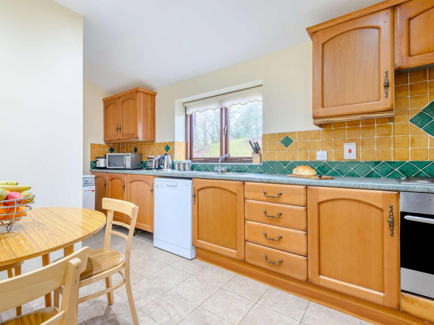 A compact kitchen with wooden cabinets, a white dishwasher, and a dining table with chairs.