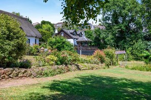 A house with a thatched roof, surrounded by a well-maintained garden with various plants and a stone wall. - 1 Bed in Paignton (oc-55119) (Paignton)