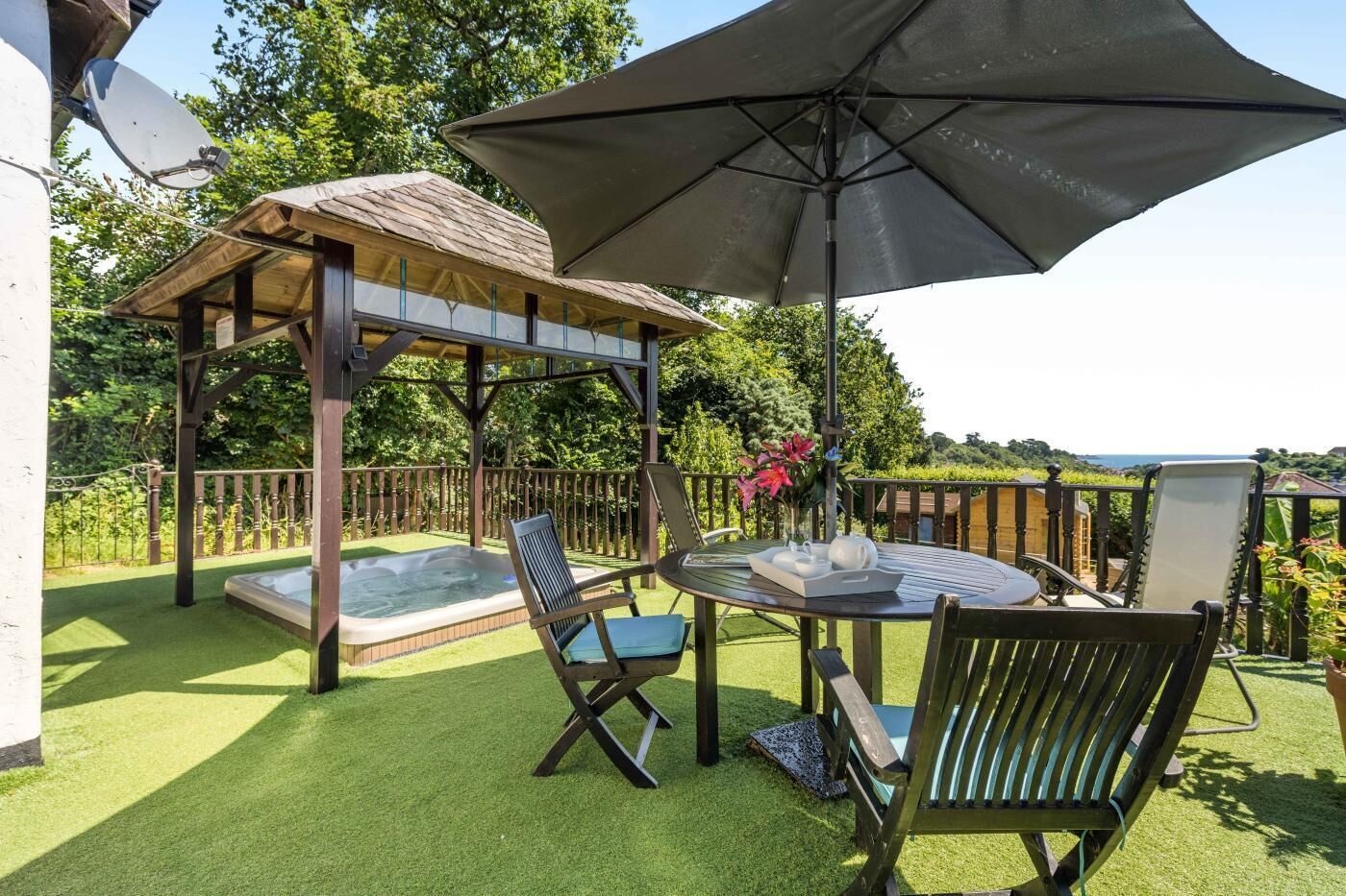Eine Außenpatio mit Whirlpool, zwei Liegestühlen, einem Tisch mit Tablett und einem großen Sonnenschirm.