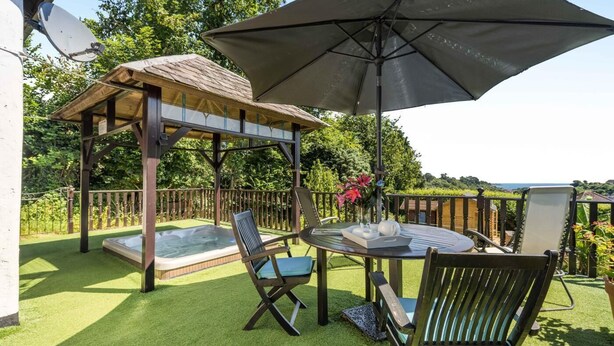 An outdoor patio with a hot tub, two lounge chairs, a table with a tray, and a large umbrella. - 1 Bed in Paignton (oc-55119) (Paignton)