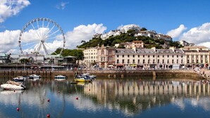 A waterfront with a Ferris wheel, boats, and buildings with a hilly backdrop. - 1 Bed in Paignton (oc-55119) (Paignton)