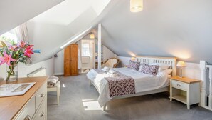A bedroom with a sloped ceiling, a bed with patterned bedding, bedside tables, a nightstand, and a wooden wardrobe. - 1 Bed in Paignton (oc-55119) (Paignton)