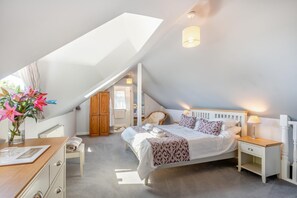 A bedroom with a sloped ceiling, a bed with patterned bedding, bedside tables, a nightstand, and a wooden wardrobe. - 1 Bed in Paignton (oc-55119) (Paignton)