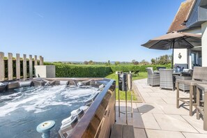 Un jacuzzi con vistas a un campo verde y un edificio con mobiliario exterior.