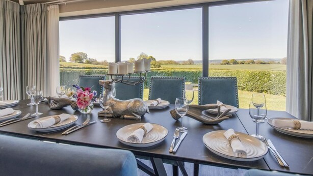 Une table à manger dressée pour quatre personnes, avec vue sur un paysage verdoyant grâce à de grandes fenêtres.