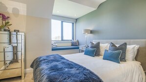 Une chambre à coucher avec un lit, un coin fenêtre aménagé en siège, un miroir et une lampe.