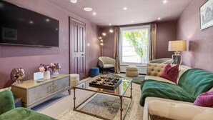 Una sala de estar con sofá, sillón, mesa de centro y televisión montada en la pared.