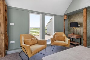 A room with two leather armchairs, a small table, and a lamp. There are large windows offering a view of a wooden structure outside. - 5 Bed in Hereford (oc-83658) (Madley)
