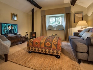 Ein gemütliches Wohnzimmer mit Fernseher, Kamin, einer Couch und einem gemusterten Hocker.