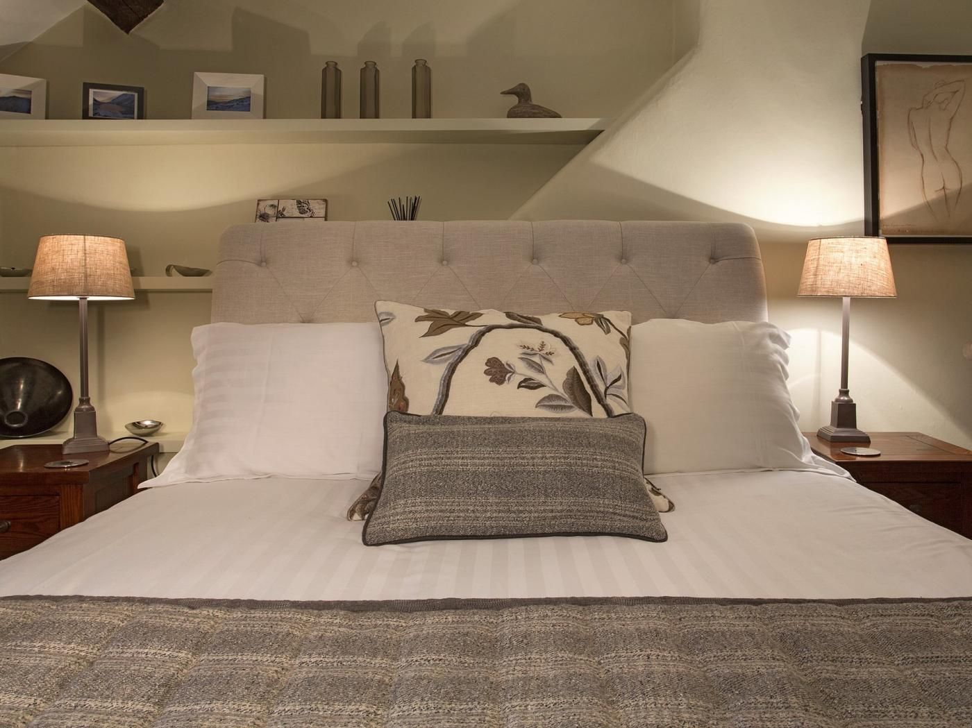 Een keurig opgemaakt bed met twee kussens, een bedlampje en een nachtkastje met een lamp.