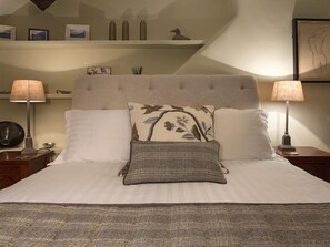Ein ordentlich bezogenes Bett mit zwei Kissen, einer Nachttischlampe und einem Nachttisch mit Lampe.