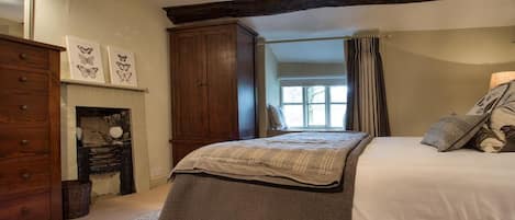Un dormitorio con cama, armario, chimenea y ventana con cortinas.