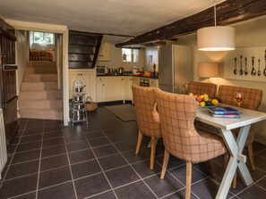 A dining area with a table, chairs, and a book. There is a kitchen in the background with cabinets and appliances. - 1 Bed in Coniston (LCC59) (Coniston)