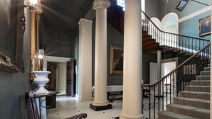 Un vaste hall d’entrée avec un escalier, de grandes colonnes et un lustre.